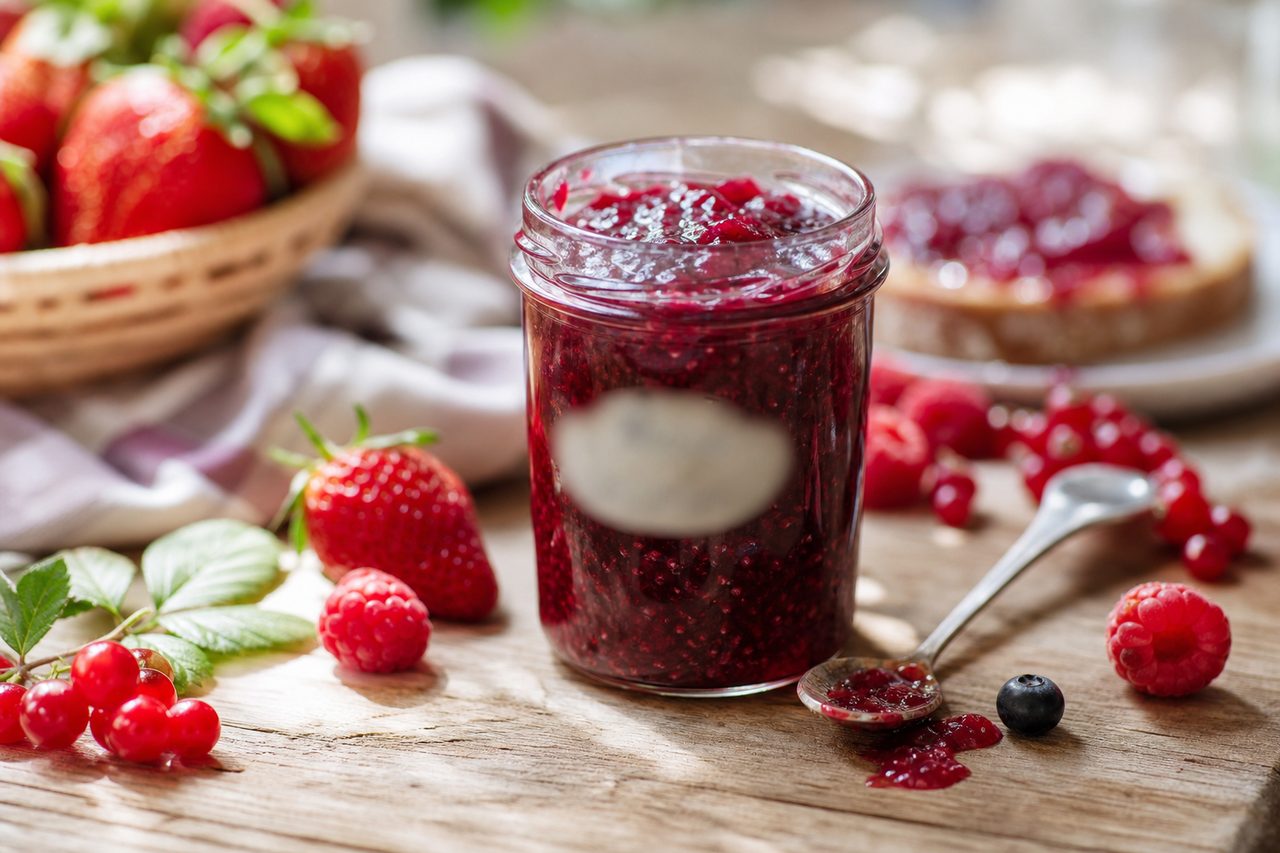 Pot de confiture ouvert avec une cuillère posée à côté sur une table en bois, fruits frais visibles