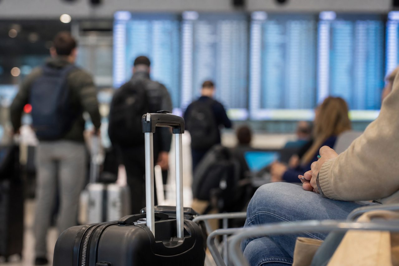Voyageurs avec bagages à main patientant dans un hall d'aéroport devant un panneau d'affichage des vols